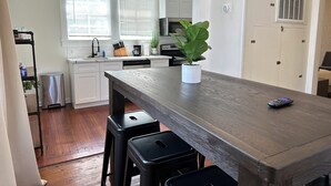 Una cocina moderna con armarios blancos, una mesa de comedor de madera, taburetes negros y una planta en maceta.