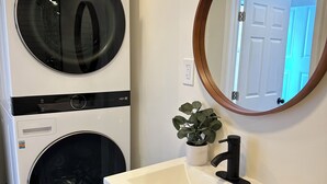Un lavadero con lavadora y secadora de carga frontal, un lavabo con espejo y una puerta que da a otra habitación.
