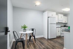 A compact kitchen with white cabinets, a white refrigerator, a stove, and a microwave. There is a small round table with two chairs and a potted plant. - Nature Lodge Studio -River - with Hiwassee River Access (Calhoun)