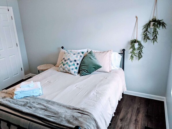 A bedroom with a bed, pillows, a bedside table, and a hanging plant.
