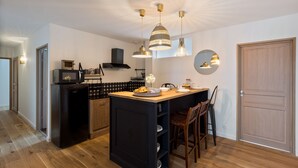 A compact kitchen with a central island, pendant lighting, and a built-in stove. - Libertitu (Bayonne)