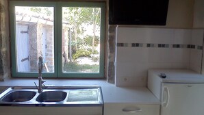 A kitchen with a double sink, a built-in stove, and a microwave. There is a window with a view of a garden. - Gorges de L'ardèche (Labeaume)