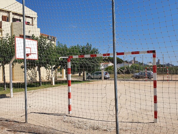 Un arco de fútbol con red, un poste a rayas rojas y blancas, y un aro de baloncesto.