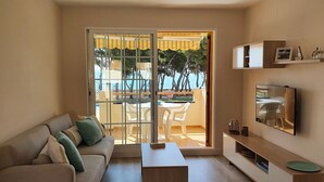 Un salon comprenant un canapé, une table basse, un téléviseur et un balcon aménagé avec du mobilier d’extérieur.