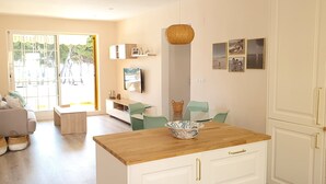Un salon moderne avec une table basse en bois, un téléviseur fixé au mur et un coin repas avec des chaises vertes.