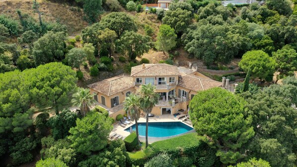 Ein zweistöckiges Haus mit Swimmingpool, umgeben von üppiger Bepflanzung und Bäumen.