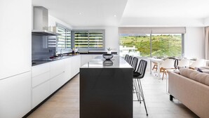 Une cuisine moderne dotée d’un îlot central, de meubles blancs et d’un coin repas offrant une vue sur la campagne.