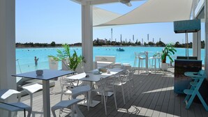 Un espace extérieur aménagé avec des tables et des chaises, offrant une vue sur une piscine et la mer.