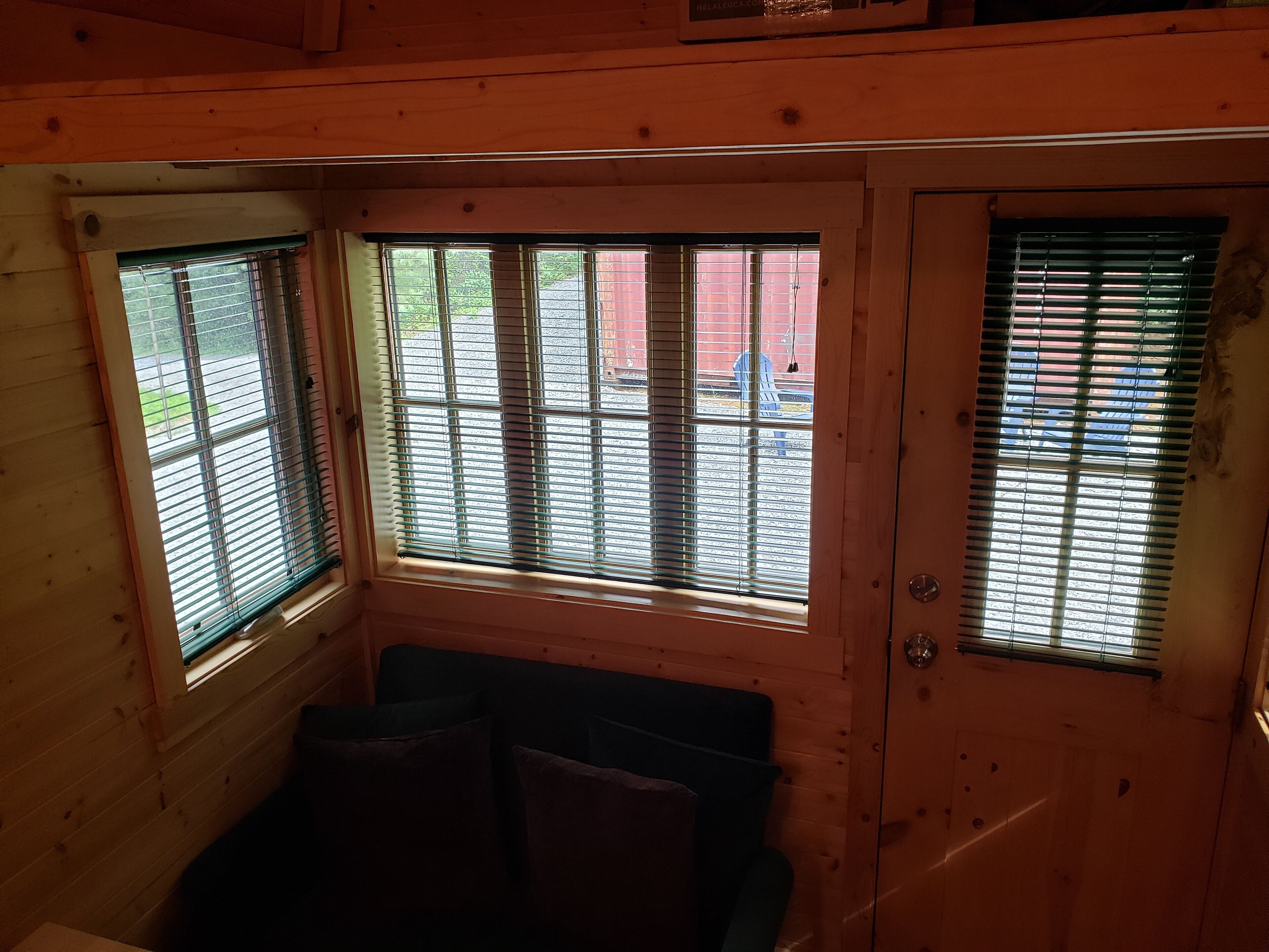 L’intérieur d’une cabane est aménagé avec du bois, il y a une fenêtre avec des stores et une porte.