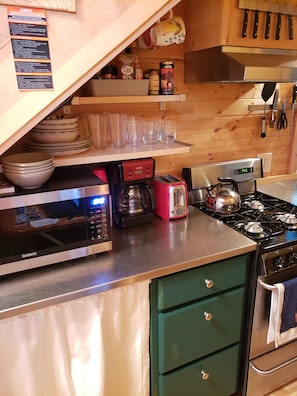 A kitchen with a Galanz microwave, a red coffee maker, a toaster, and a stove. - The Tumbleweed Tiny House (Zirconia)