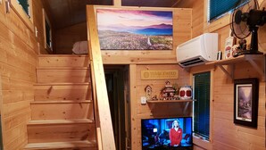 A wooden cabin interior with a staircase, a television, a small table, and a chair. - The Tumbleweed Tiny House (Zirconia)