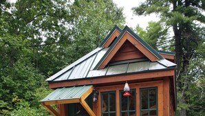 A wooden cabin with a green door, windows, and a small porch with steps. - The Tumbleweed Tiny House (Zirconia)