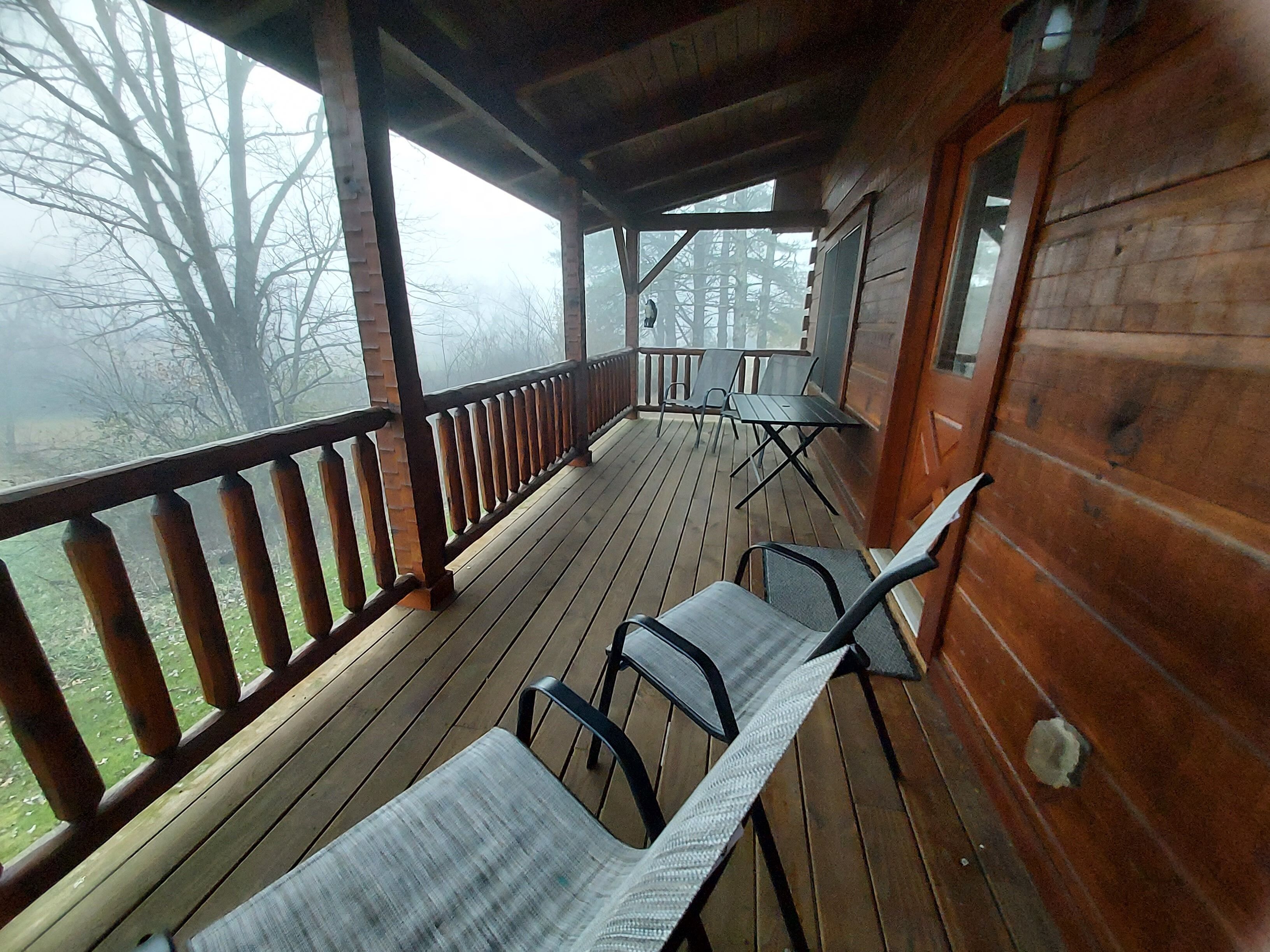 A wooden deck with a railing, two tables, and four chairs.
