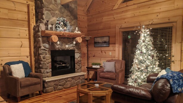 A cozy log cabin interior with a stone fireplace, leather furniture, and a decorated Christmas tree. - Tranquility at Fall Creek Falls (Spencer)