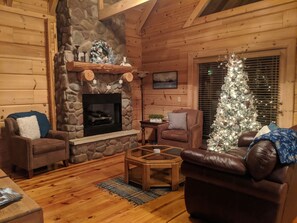A cozy log cabin interior with a stone fireplace, leather furniture, and a decorated Christmas tree. - Tranquility at Fall Creek Falls (Spencer)