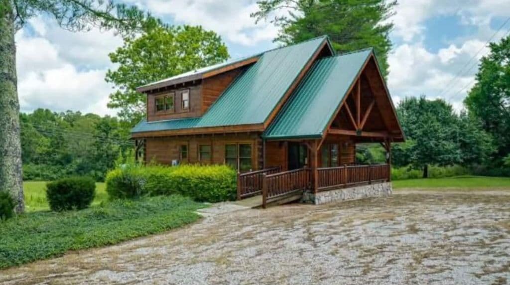 Une cabane en rondins à deux étages, avec un toit en métal vert et une véranda.