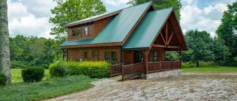 A two-story log cabin with a green metal roof and a porch.