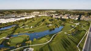 An aerial view of a golf course with water hazards, sand bunkers, and a residential area in the background. - Rehoboth/Lewes Townhouse Pond View, Community Pool, Golf & 10-Min Drive to Beach (Rehoboth Beach)