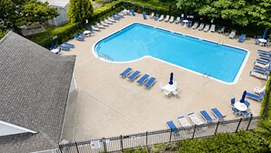 A rectangular swimming pool surrounded by lounge chairs and umbrellas, with a fence and greenery in the background. - Rehoboth/Lewes Townhouse Pond View, Community Pool, Golf & 10-Min Drive to Beach (Rehoboth Beach)