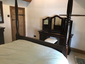 A bedroom with a four-poster bed, a wooden dresser with a mirror, and a door in the background. - Village Period Cottage Next to a Idyllic Stream (Coventry)
