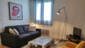 A modern living room with a sofa, a coffee table, a yellow chair, a TV, and a lamp. - HAPPY KOOL | city center | wifi | private parking (Blois)