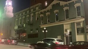 Een historisch gebouw met een klokkentoren, grote ramen en een straatbeeld met geparkeerde auto's.