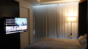 Une chambre d’hôtel avec un lit, un téléviseur diffusant le film « Hunger Games », une lampe et un rideau.