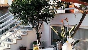 Ein Essbereich im Freien mit einem für zwei Personen gedeckten Tisch, umgeben von Stühlen, unter einer Holzw pergola.