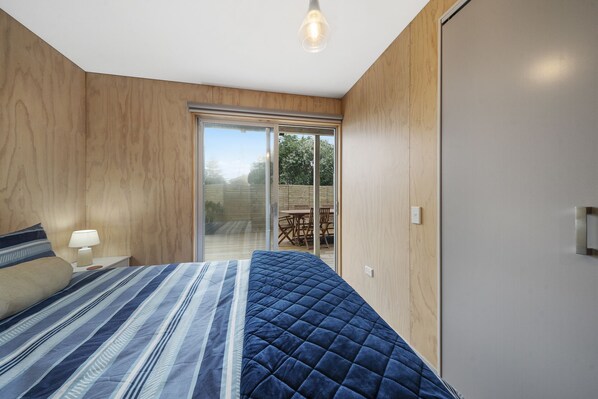 A bedroom with a bed, a nightstand, a lamp, a sliding glass door leading to an outdoor area with a table and chairs.