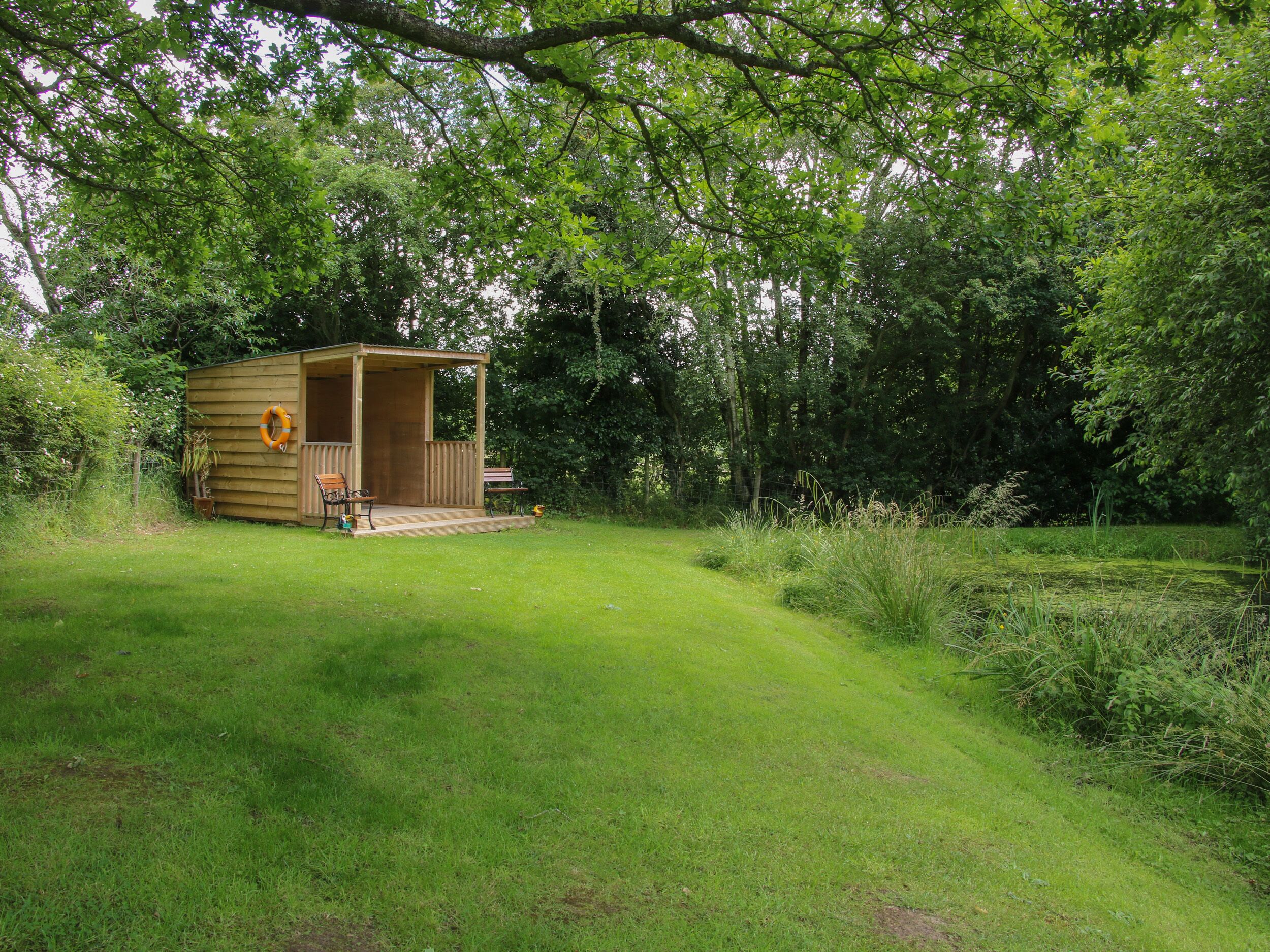 Eine kleine Holzhütte mit Veranda und Bank, umgeben von üppiger Vegetation.