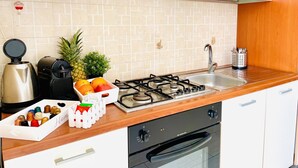 Una cocina con estufa a gas, lavamanos y cafetera. Hay frutas y un juego de té en la encimera.