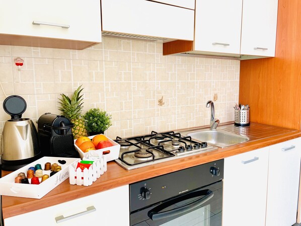 A kitchen with a gas stove, sink, and a coffee maker. There are fruits and a tea set on the counter.