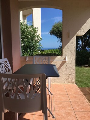 A patio with a table and chairs, a view of the sea, and a garden.