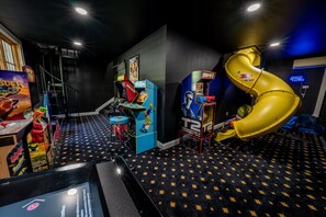 Ein Spielsalon mit verschiedenen Automaten, darunter eine gelbe Rutsche, und einem teppichartigen Boden mit Sternenmuster.