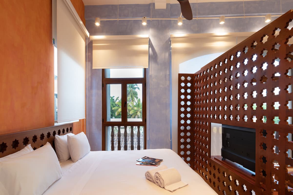 A hotel room with a bed, a television, and a view of palm trees through the window.