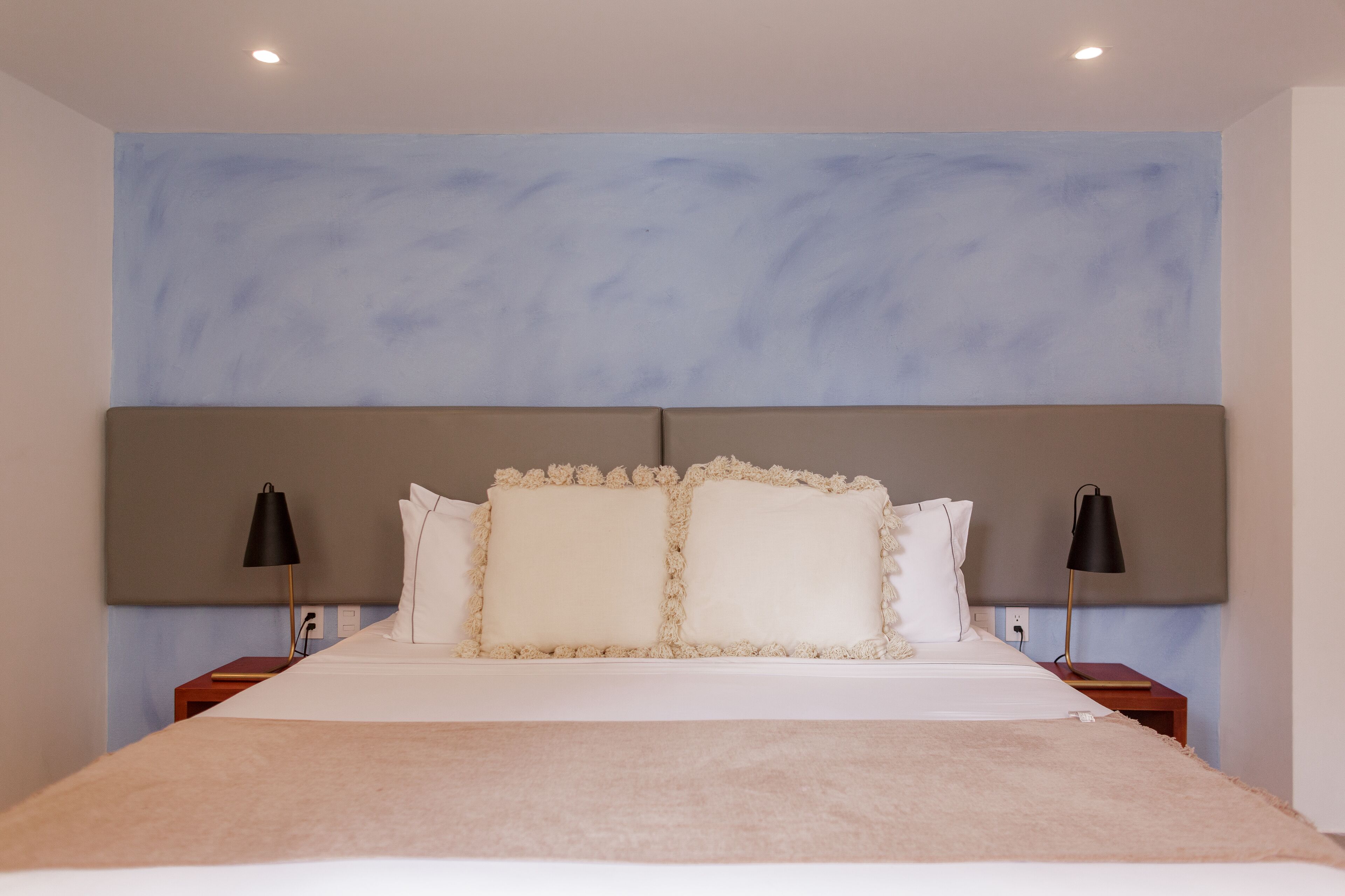 A neatly made bed with a beige blanket, two bedside lamps, and a headboard with a textured design.
