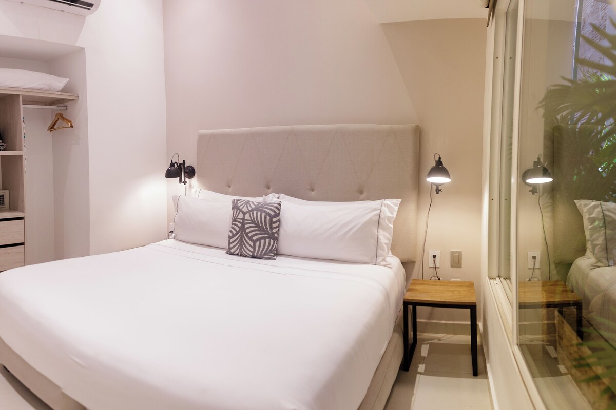 A neatly made bed with a headboard, bedside tables, and a hanging light fixture.