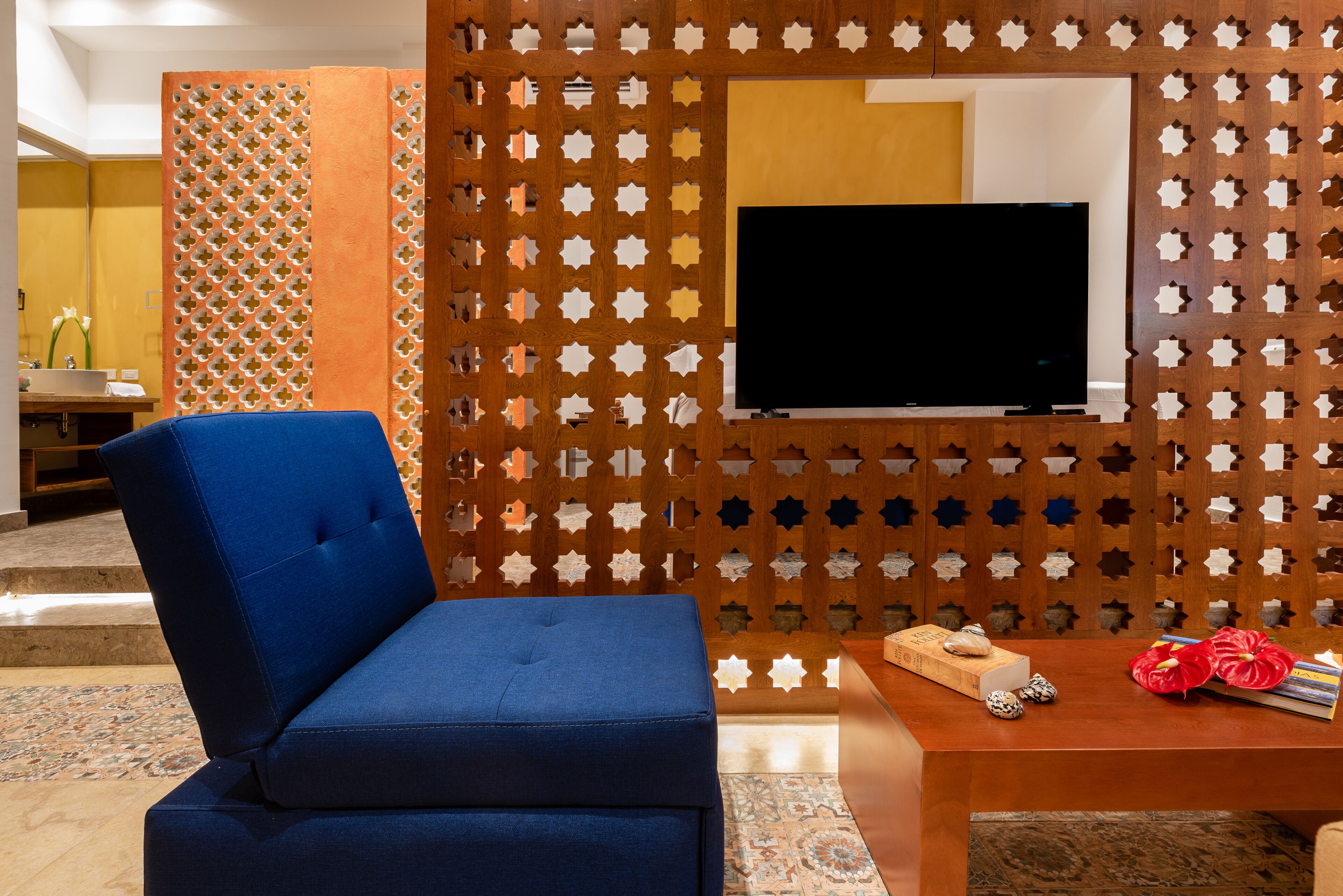 A blue sofa, a wooden table with a book and decorative items, and a TV mounted on a wall with a geometric pattern.