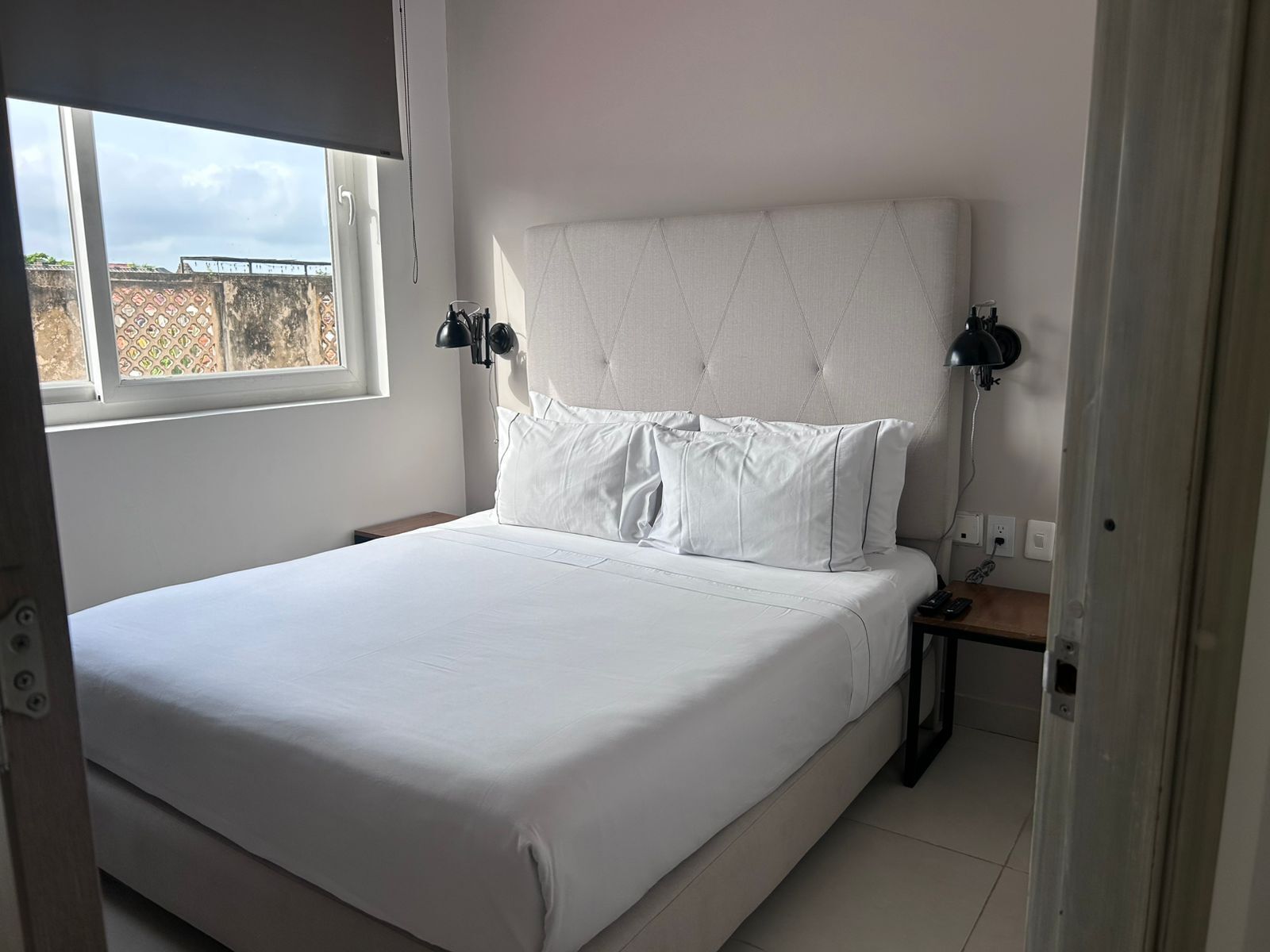 Un lit bien fait, avec du linge de lit blanc, une tête de lit capitonnée et deux lampes de chevet.
