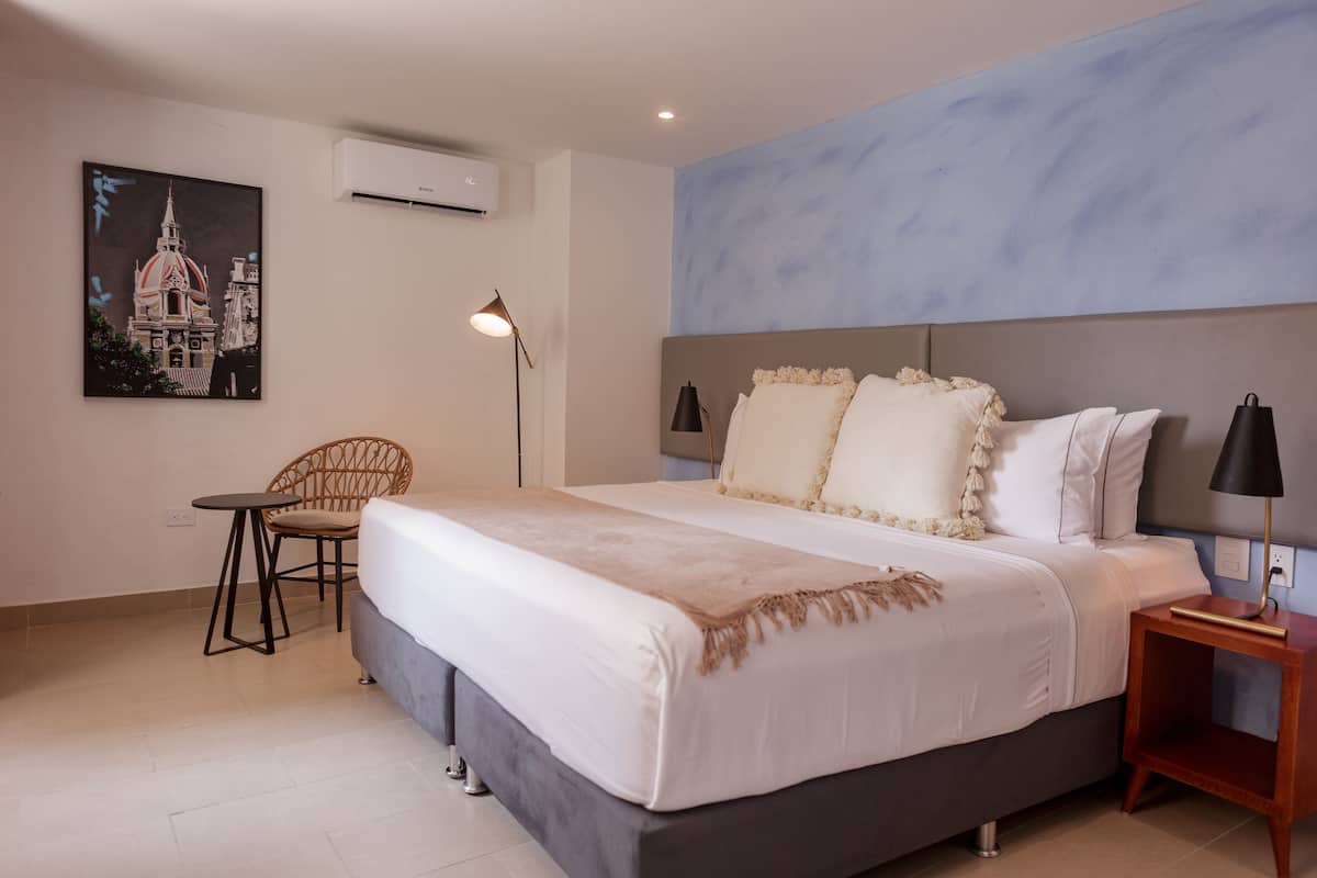 A bedroom with a large bed, a chair, a small table, and a painting on the wall.