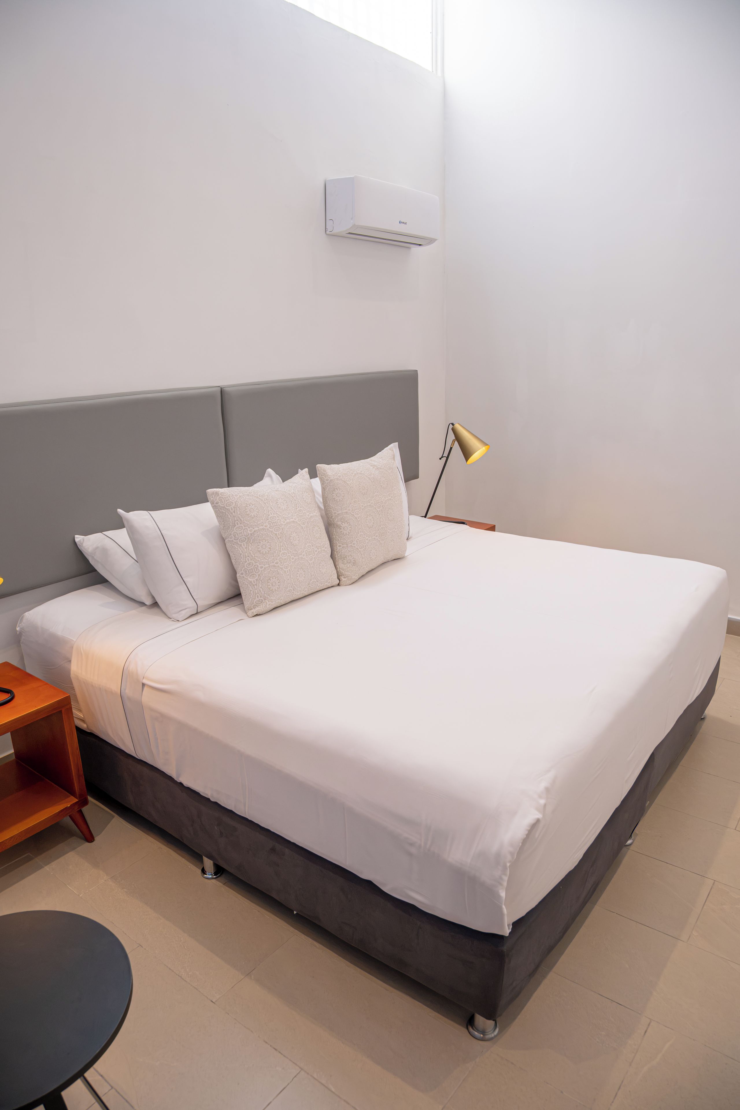 Ein modernes Schlafzimmer mit Bett, Nachttischen, einer Lampe und einer Wand-Klimaanlage.