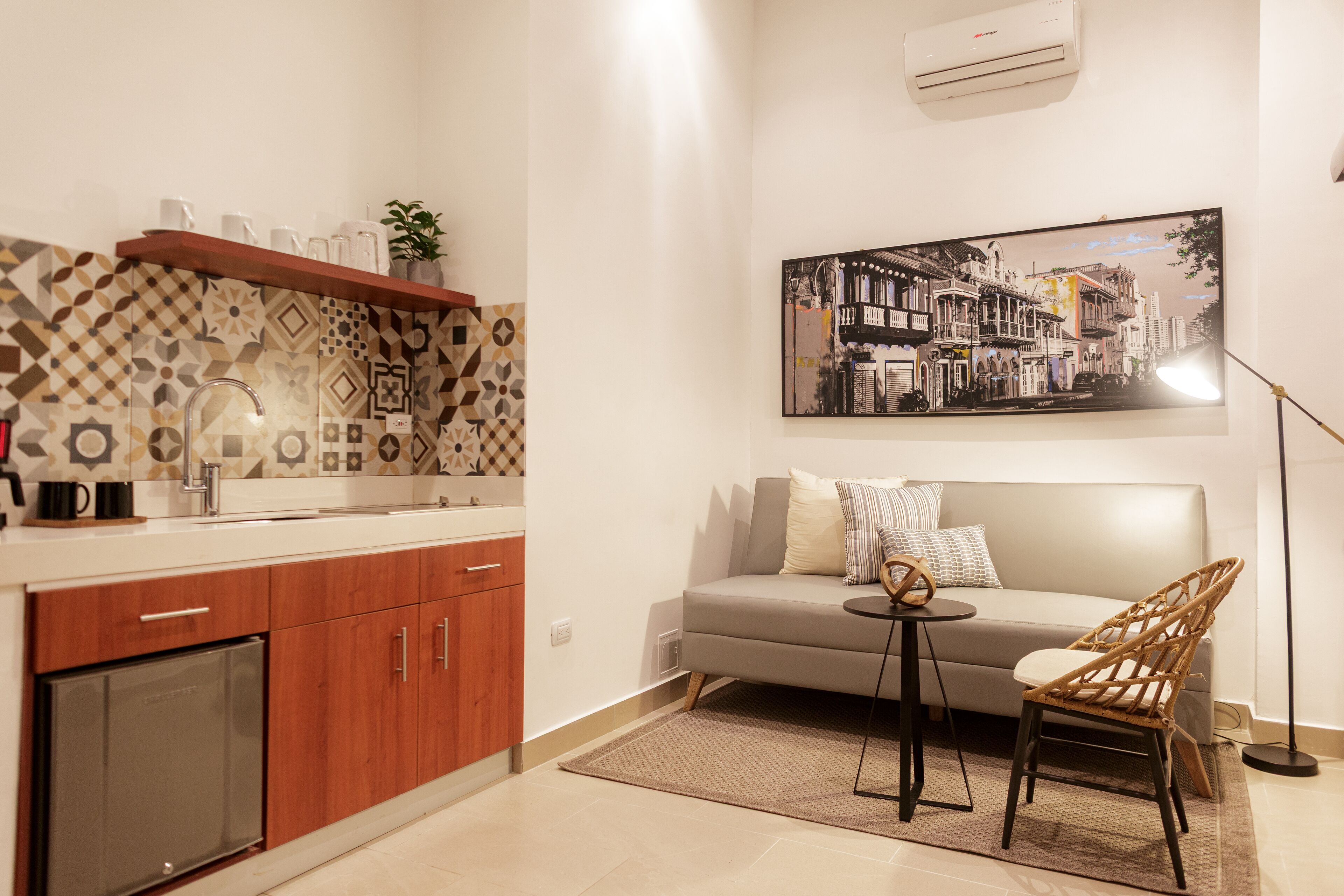 A modern kitchen with patterned backsplash, wooden cabinets, and a built-in dishwasher. A dining area with a sofa and chair is adjacent to the kitchen, featuring a small round table.