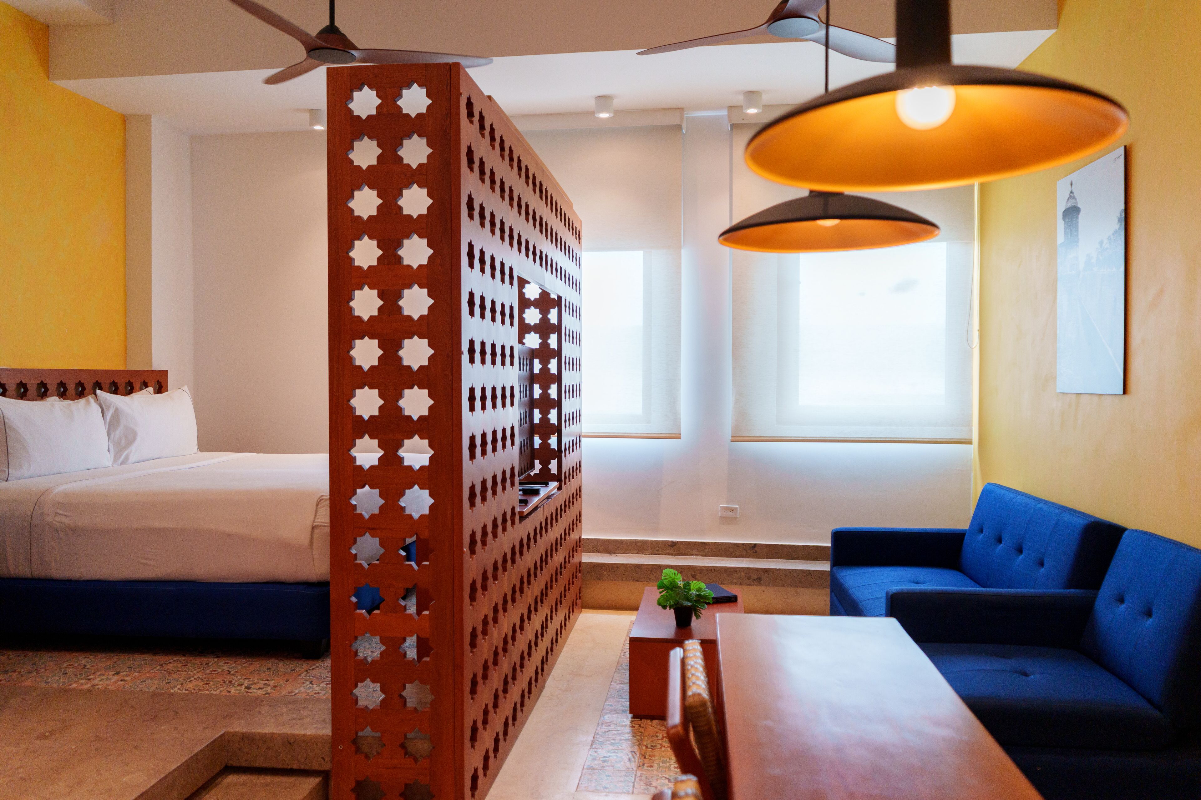 A hotel room with a bed, a blue sofa, a wooden partition with star cutouts, and a ceiling fan.