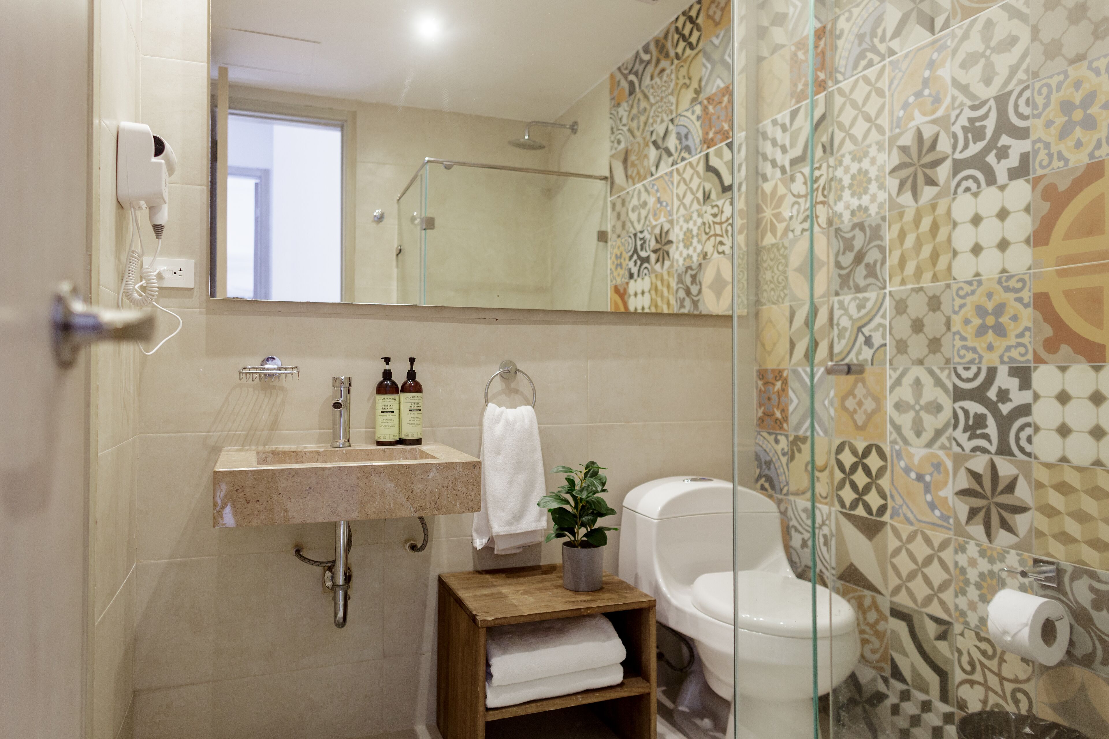 A bathroom with a sink, mirror, toilet, and patterned tiles.