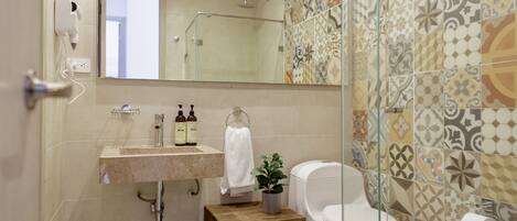 A bathroom with a sink, mirror, toilet, and patterned tiles.