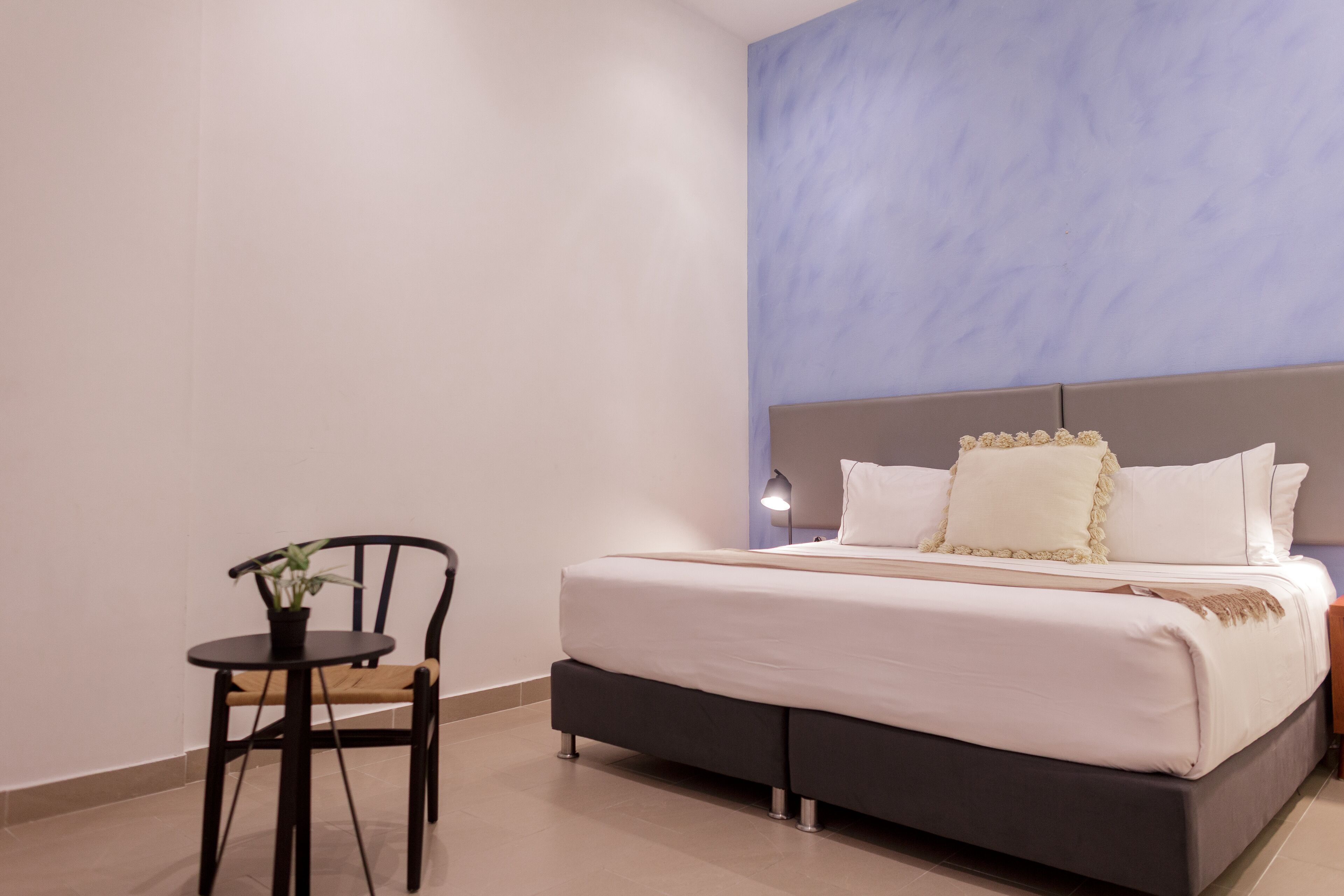 A bedroom with a bed, bedside table, lamp, chair, and a small table with a plant.