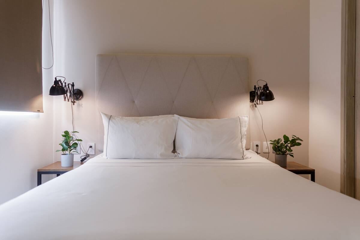 A neatly made bed with a tufted headboard, two bedside tables with lamps, and potted plants.