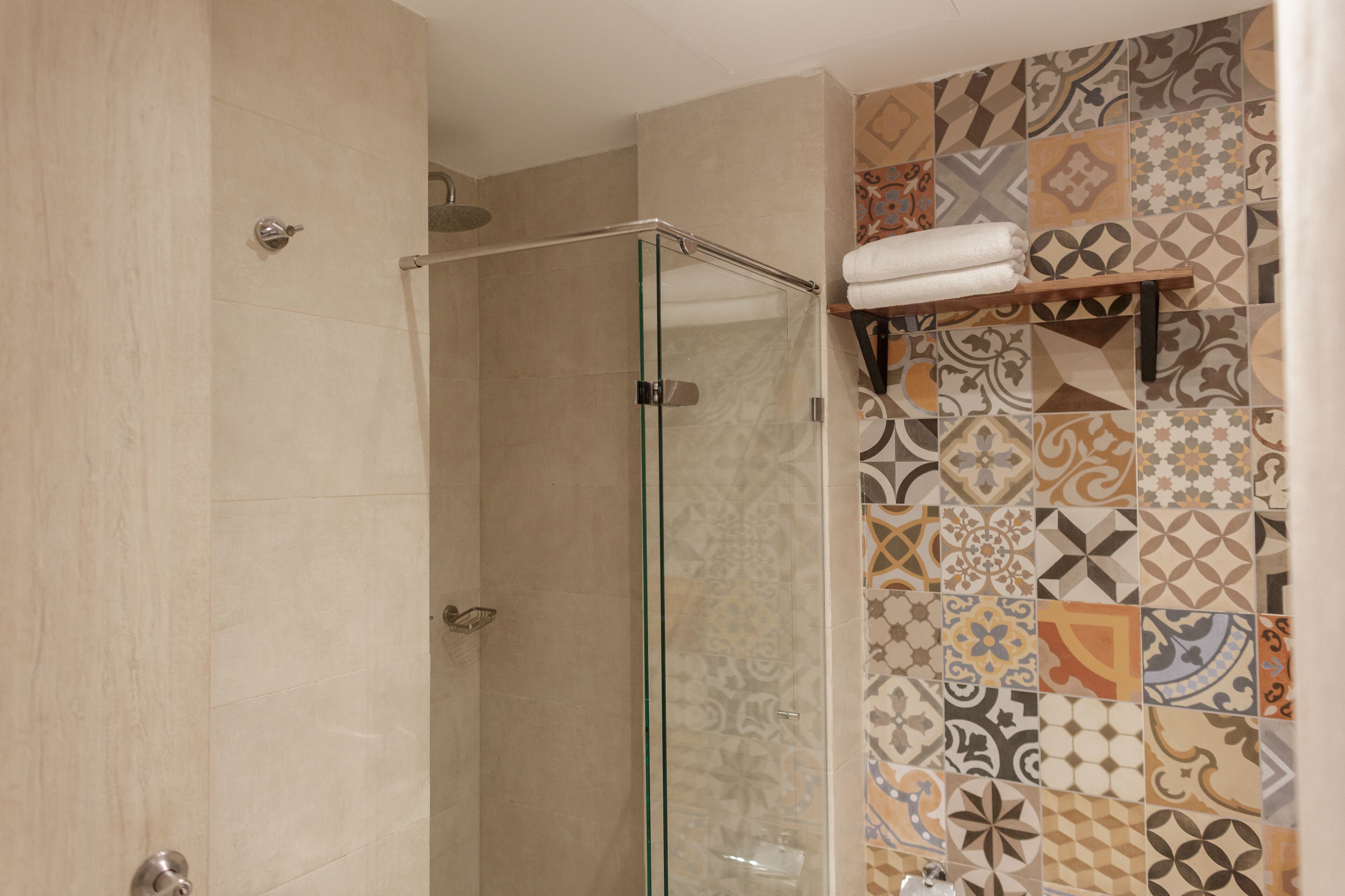 A shower with a glass door, a towel rack with towels, and a wall with patterned tiles.