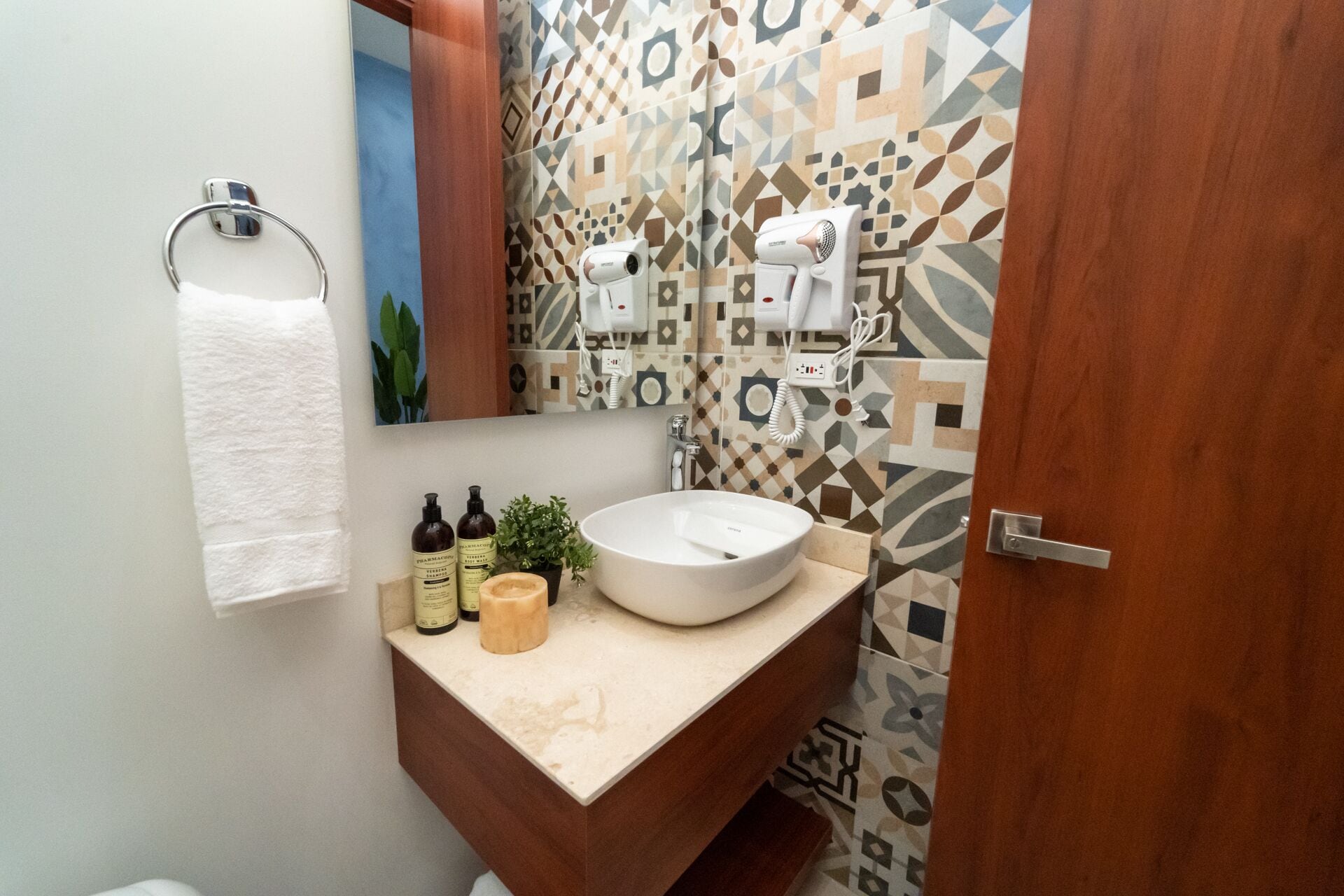 Un baño con lavamanos blanco, tocador de madera, perchero y espejo.