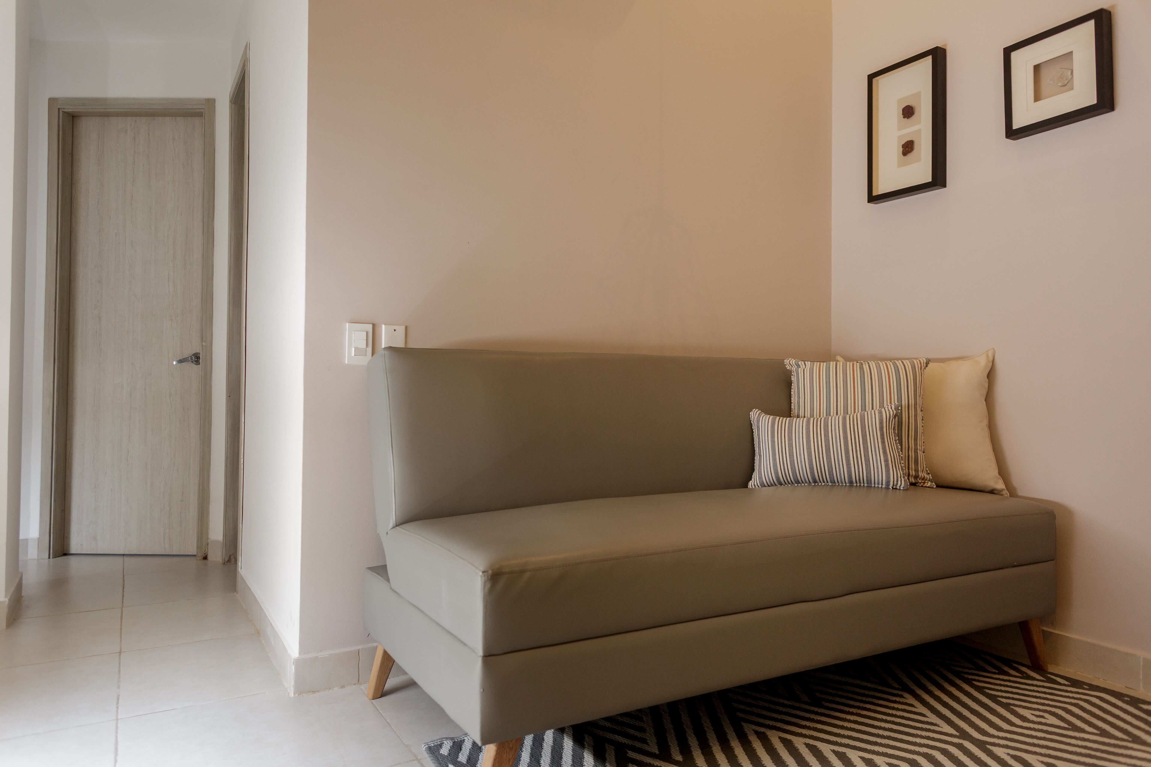 Un sofá de tonos neutros con almohadones a rayas, una alfombra estampada y una puerta en un pasillo con un interruptor de luz en la pared.
